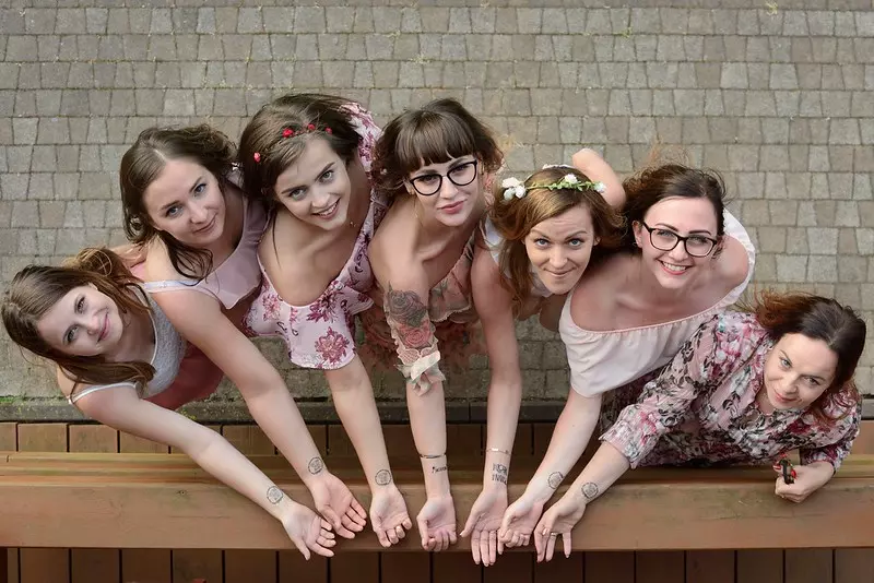 Fotografia rozbawionych na wieczorze panieńskim dziewczyn pokazujących swoje tatuaże na nadgarstkach