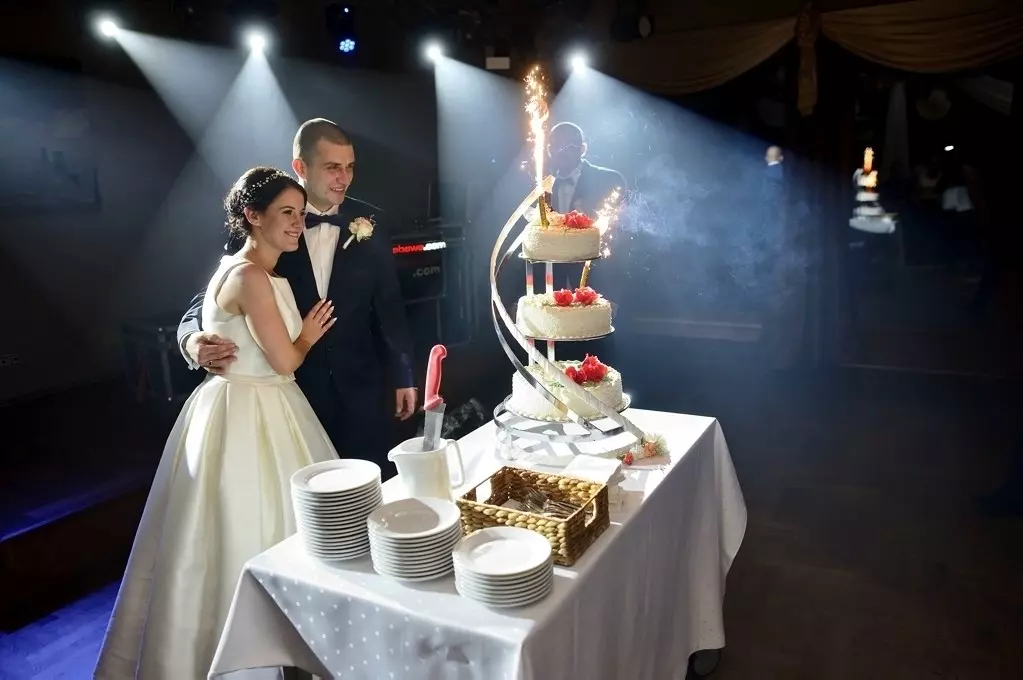 Młoda Para patrząca na swój wymarzony tort ślubny na tle refleksów świetlnych przedzierających się przez sceniczny dym