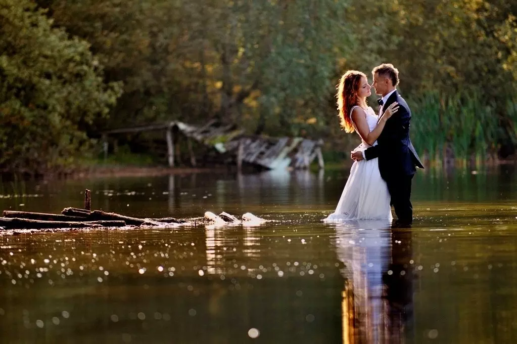 Fotografia eksponująca ślubną parę na środku płytkiej zatoczki jeziora