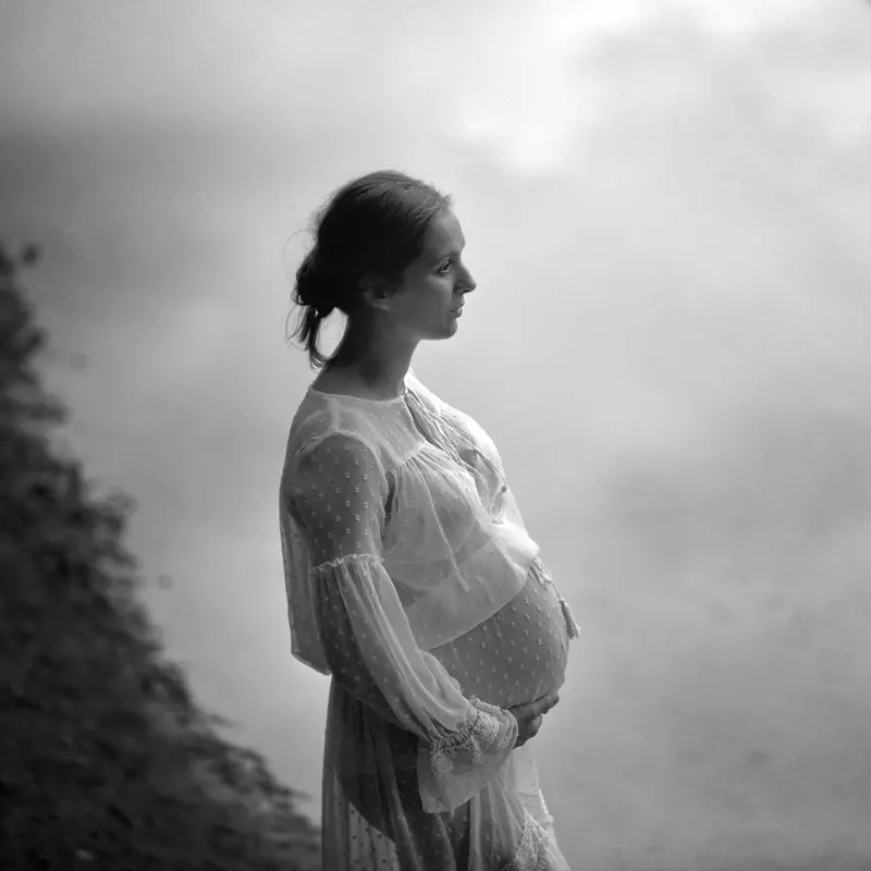 Portret czarnobiały dziewczyny w ciąży na tle spokojnego jeziora odbijającego chmury