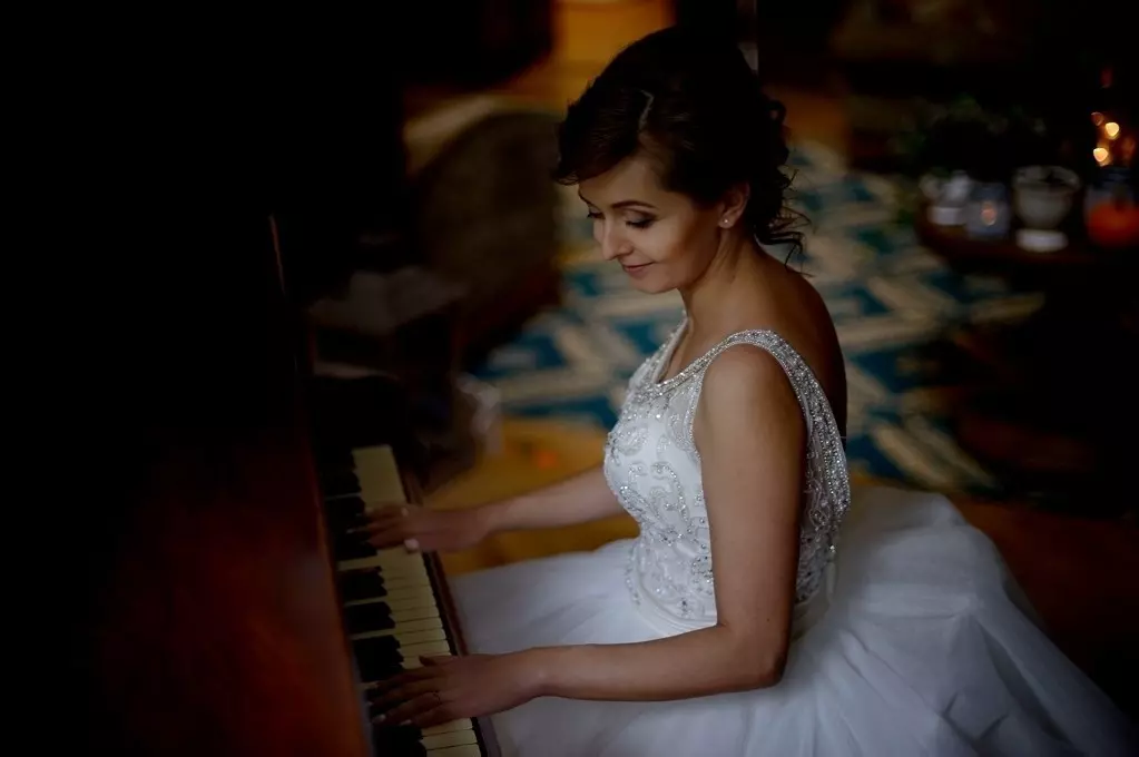 Panna młoda w sukni ślubnej grająca na zabytkowym fortepianie