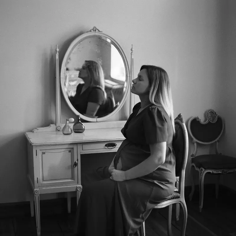 Modelka w ciąży siedząca na starym krześle przed lustrem