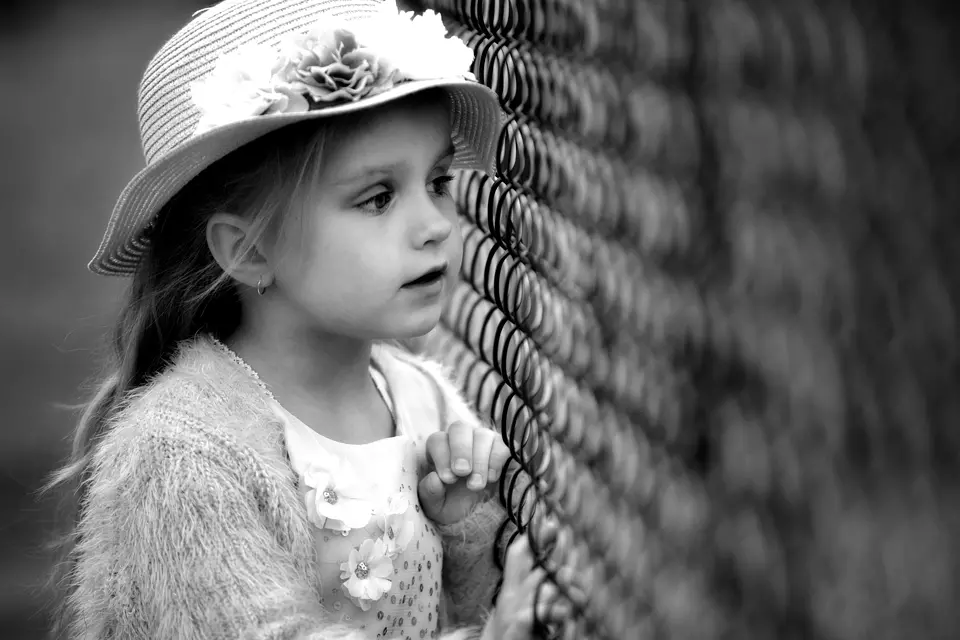 mała dziewczynka patrząca z obawą przez siatkę ogrodzenia z drutu
