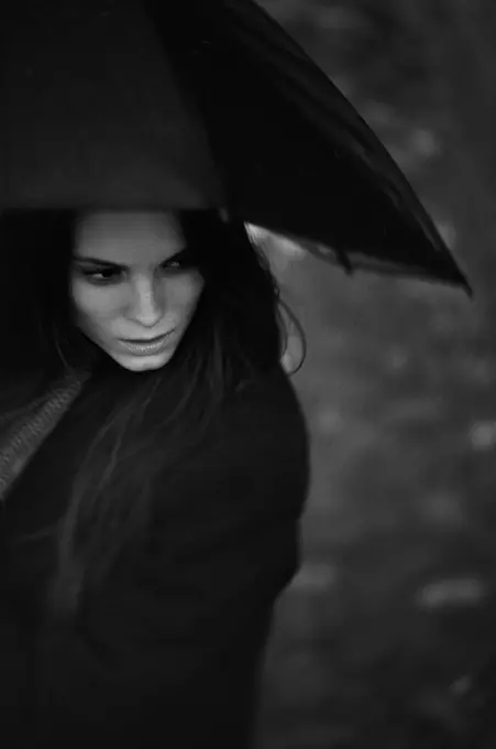 Artystyczna fotografia portretowa modelki patrzącej przez podniesiona parasolkę