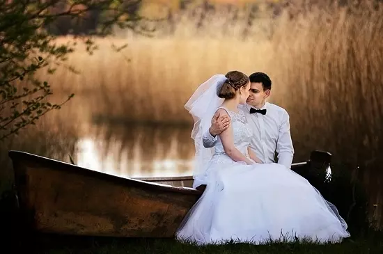 Para ślubna siedząca na burcie łodzi na tle trzcin i jeziora