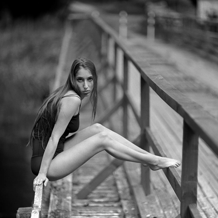 Siedząca dziewczyna na poręczy starego mostu na rzece ubrana w czarne body