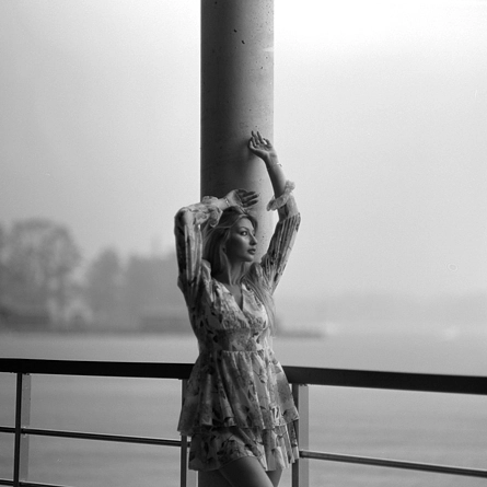 Kobieta pozująca pod pomostem na tle jeziora i deszczu
