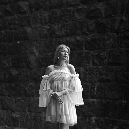 Kobieta o bląd włosach stojąca przed kamienną ścianą