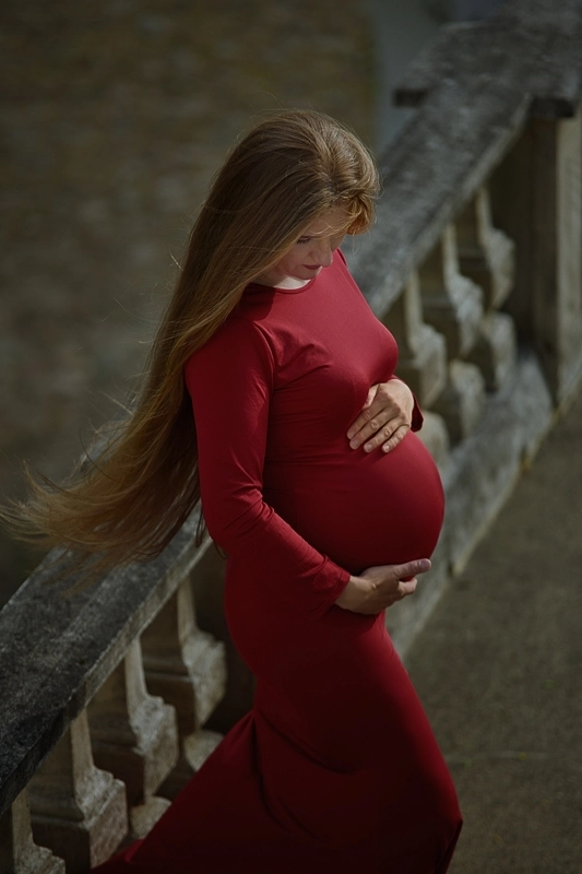Kobieta w ósmym miesiącu ciąży pozujaca w czerwonej sukni na tarasie Zamku Podewils w krągu