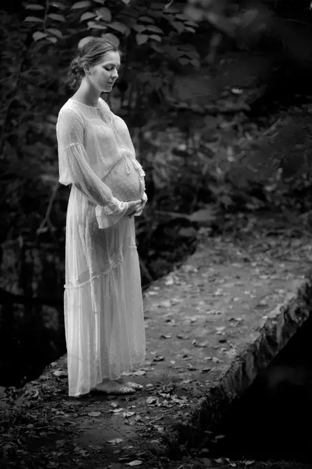 Stojąca boso na betonowym starym moście kobieta w 9 miesiacu ciąży