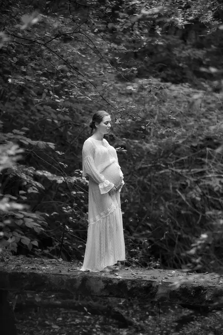 Kobieta w zaawansowanej ciąży pozująca do zdjęć w pięknej prześwitującej sukni