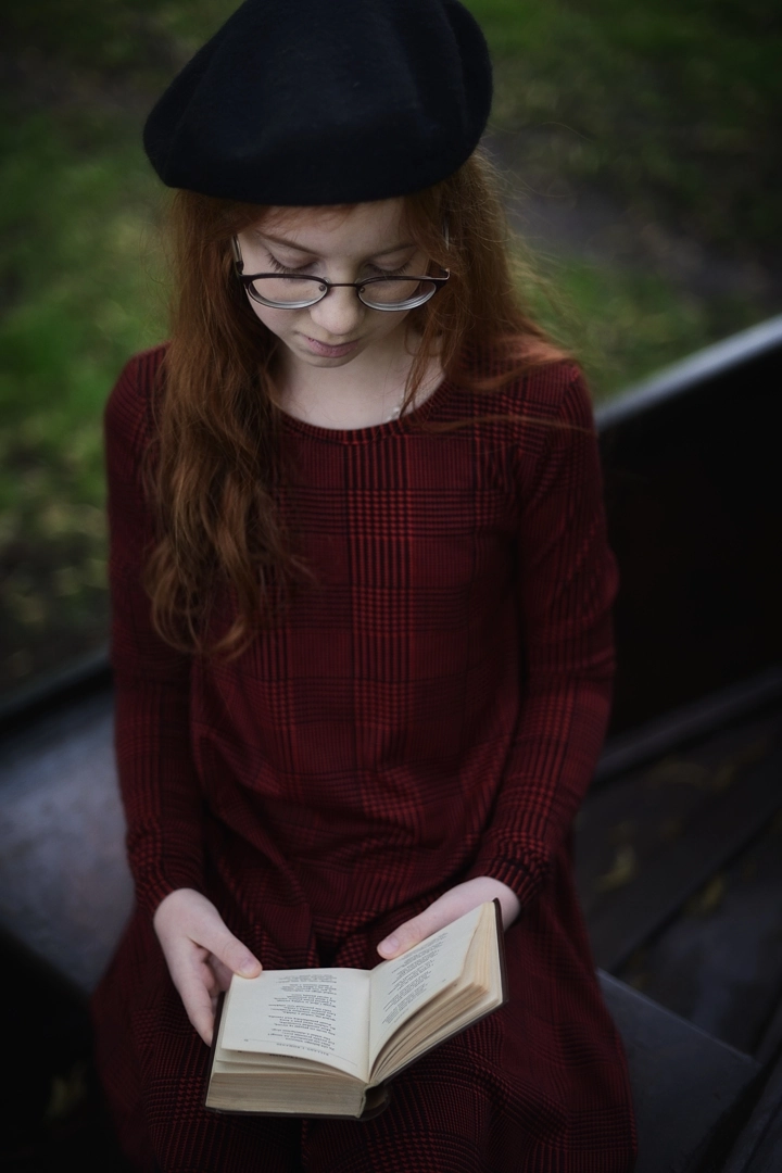 Portret rudowłosej dziewczynki w okularach czytającej książkę