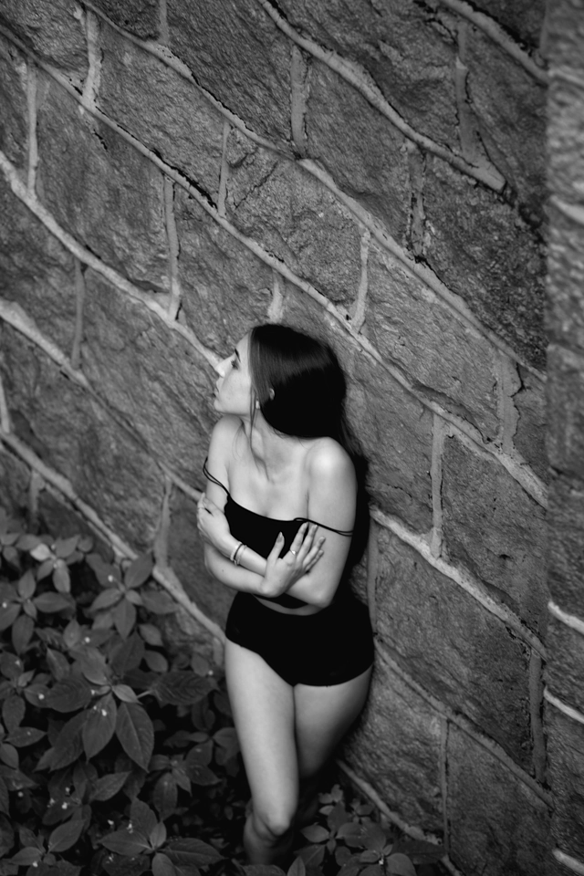 Dziewczyna w czarnym body ukazująca swe ramiona na tle ściany wiaduktu