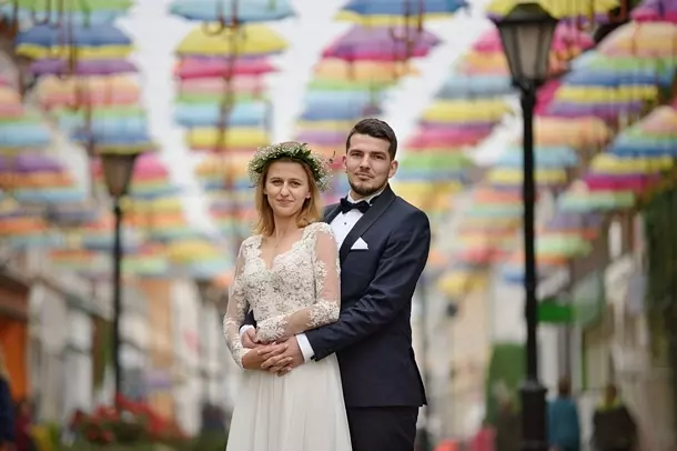 Małżonkowie wtuleni w siebie na tle setek wiszących parasolek w Połczynie Zdroju